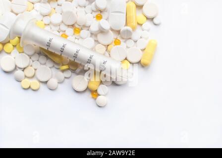 Ein Haufen gelber und weißer Tabletten, auf weißem Hintergrund isolierte Pillen mit Spritze. Nahaufnahme. Selektiver Fokus. Gesundheitstag. Copyspace Stockfoto