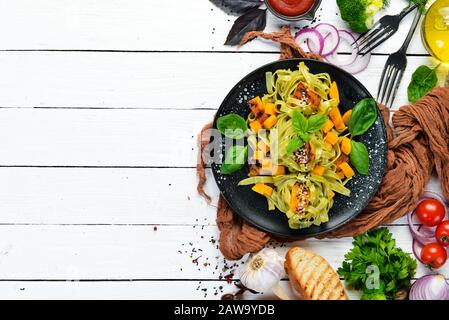 Pasta mit Kürbis und Spinat in einem schwarzen Teller auf weißem Holzhintergrund. Draufsicht. Freier Speicherplatz für Ihren Text. Stockfoto