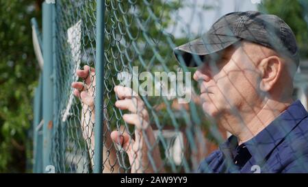 Bild mit einem Verzweifelten Mann, Der Besorgt Hinter einer Metallischen Mauer blickt, Gefängniskonzept Stockfoto