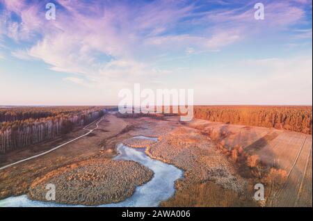 Blick auf die Landschaft und den gefrorenen Bach am Abend bei Sonnenuntergang. Schöne Naturlandschaft mit bewölktem Himmel. Malerische Landschaft Stockfoto