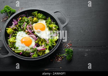 Gemüse-Shakshuka in einer Pfanne. Spiegeleier mit Gemüse: Brokkoli, grüne Erbsen, Bohnen, Zwiebeln. Draufsicht. Freier Speicherplatz für Ihren Text. Stockfoto