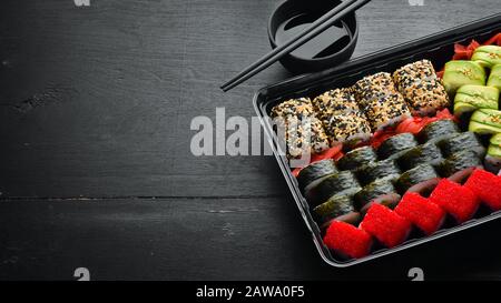 Lieferung von Speisen, Sushi-Brötchen. Set Sushi in einer Kunststoffbox. Traditionelle Japanische Küche. Draufsicht. Rustikaler Stil. Stockfoto
