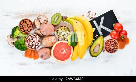 Lebensmittel, die natürliches Kalium enthalten. K: Kartoffeln, Pilze, Banane, Tomaten, Nüsse, Bohnen, Brokkoli, Avocados. Draufsicht. Auf weißem Holzhintergrund. Stockfoto