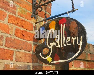 Eine bunte Künstlerpalette mit dem Wort "Galerie" hängt an einer Ziegelwand, um für ein für Besucher offenes Künstleratelier zu werben. Stockfoto