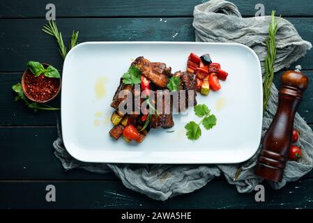 Gebackene Schweinerippen mit Gemüse. In der Platte. Auf Holzgrund. Draufsicht. Freier Speicherplatz für Ihren Text. Stockfoto
