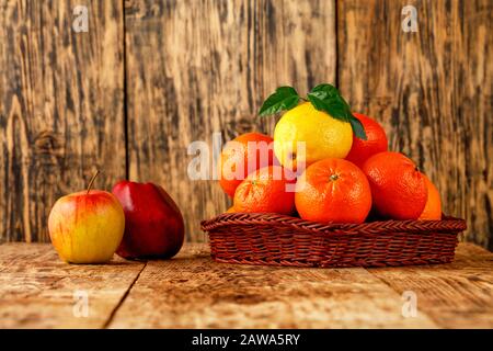 Tangerinen und Zitrone in einem Korbkorb liegen rote Äpfel auf einem alten Holztisch. Stockfoto