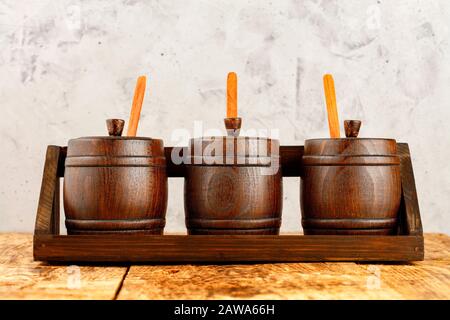 Set aus kleinen Holzfässern zur Lagerung von Getreide in einem Holztablett auf einem alten Holztisch vor grauem Betonboden. Stockfoto