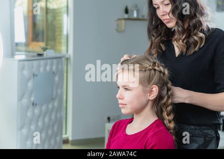 Friseursalon verwebt einem blonden Mädchen der Preteen ein Geflecht Stockfoto