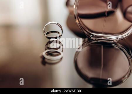 Schließen Sie die goldenen Ringe der Hochzeit mit Parfüm auf einem Glastisch. Vorbereitung der Hochzeit. Kopierraum. Stockfoto
