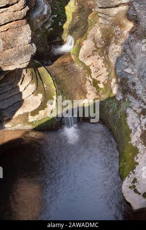 Gebirgsbach, der durch den engen, felsigen Schlitzschlucht, über Felsen, die von grünem Moos bedeckt sind, von der Sonne erhellt wird Stockfoto