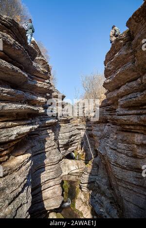 Zwei Bergwanderer stehen an der Spitze einer felsigen Klippen, beide Seiten am Eingang des erstaunlichen Canyon mit Bergbach über moosigen Felsen fließt Stockfoto