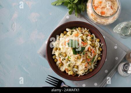 Gesunder Salat aus Sauerkraut, Erbsen aus Dosen und einem apfel in einer Schüssel auf hellblauem Grund, Draufsicht Stockfoto