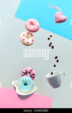 Konzept zum Valentinstag, Levitation von Douglasien über der herzförmigen Schüssel. Kaffeebohnen, die in einer Espresso-Tasse fliegen. Hand fängt pinkfarbenen Donut. Kreativer Bac Stockfoto