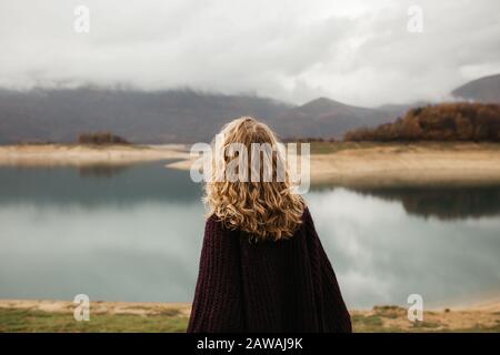 Glückliches Mädchen mit lockig blonden Haaren tanzt allein auf einem See, ihr Haar flieht wegen des Windstroms, frei als Vogel. Foto von Mädchen mit lockigem Haar ST Stockfoto