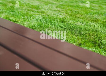 Abstrakter geometrischer Hintergrund mit einer braunen Bank in einem grünen Park über grünem Rasengras. Makroaufnahme mit selektivem Fokus und flachem Freiheitsgrad Stockfoto