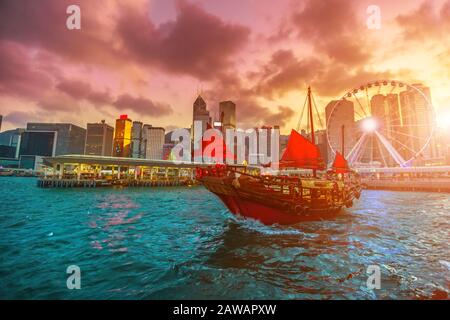 Trödelboot bei Sonnenuntergang mit Wolkenkratzern und Gebäude der Skyline der Stadt Hongkong in China. Stockfoto