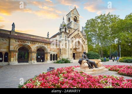 Eine bronzene Statue eines Mannes liegend auf einer Bank durch Blüten vor einem mittelalterlichen Gebäude in die Burg von Vajdahunyad in Budapest Ungarn umgeben Stockfoto