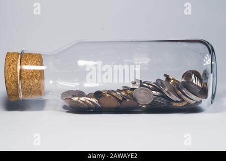 Glasbecher mit Korkstopfen und gefüllt mit internationalen Münzen aus verschiedenen Ländern. Transparente Moneybox. Finanzspeicherkonzept Stockfoto