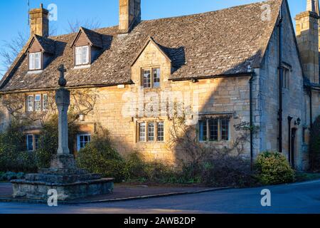 Cross Cottage mit mittelalterlichen Kreuz am Nachmittag Wintersonne. Stanton, Cotswolds, Gloucestershire, England Stockfoto