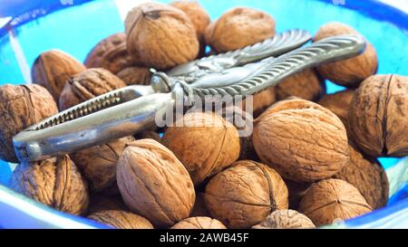 Walnüsse in der Schale mit einem Nußhörnchenknacker, in einer blauen Glasschüssel Stockfoto