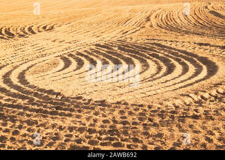 Muster von gebogenen Graten und Furchen auf einem sandigen Feld. Spuren auf dem Sand. Traktorbahnen Stockfoto