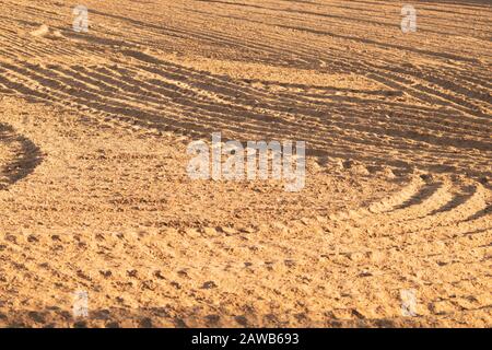 Muster von gebogenen Graten und Furchen auf einem sandigen Feld. Spuren auf dem Sand. Traktorbahnen Stockfoto