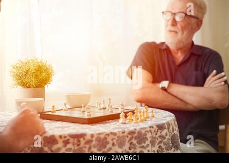 Cleverer Ältester mit Schachbrettspiel zu Hause Pflege für gesundes Gehirnkonzept Stockfoto