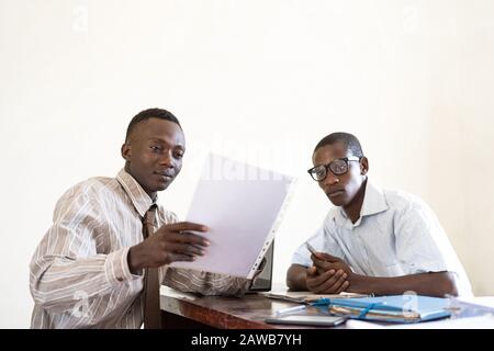 Zwei echte afrikanische Geschäftsleute diskutieren über Papierbogen mit Dokumenten und Text Stockfoto
