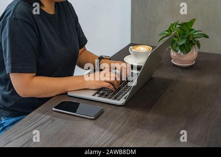 Die Hände der Frau tippen Laptop neben dem Smartphone auf Holztisch Stockfoto