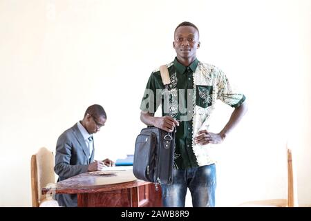 Stolzer Junger afrikanischer Student, der nach dem Lebenslauf in seinem zukünftigen Büro steht und im Hintergrund mit einem Geschäftsmann interviewt wird Stockfoto