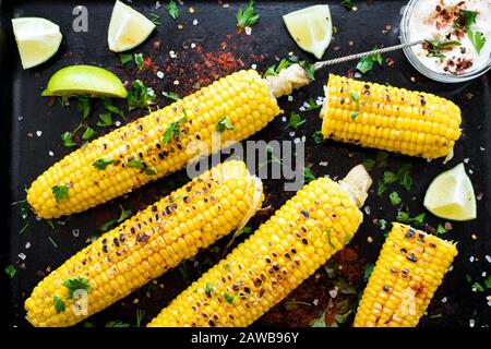 Gegrillte Maiskolben im mexikanischen Stil mit Kalk, Cilantro, Chili und weißer Soße auf schwarzem Grund. Draufsicht. Stockfoto