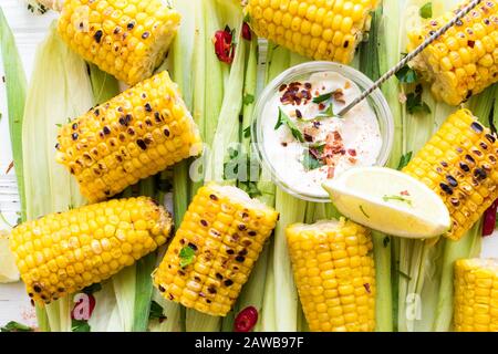 Gegrillte Maiskolben im mexikanischen Stil mit Kalk, Cilantro, Chili und Sauce auf weißem Holzhintergrund. Draufsicht. Nahaufnahme. Stockfoto