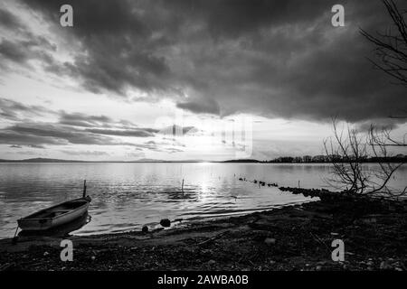 Ein leeres kleines Boot im Trasimeno-See (Umbrien, Italien) bei Sonnenuntergang, in der Nähe von Skelettpflanzen Stockfoto