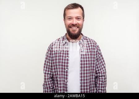 Portrait des fröhlichen gutmütigen bärtigen jungen Mannes in legeren Kragenhemden, das mit freundlichen Grüßen auf der Kamera steht und zufrieden mit dem Leben aussieht. In Stockfoto