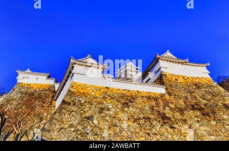 Vier weiße Türme haben hohe Steinmauern der Burg Himeji in Japan unter blauem Himmel. Stockfoto