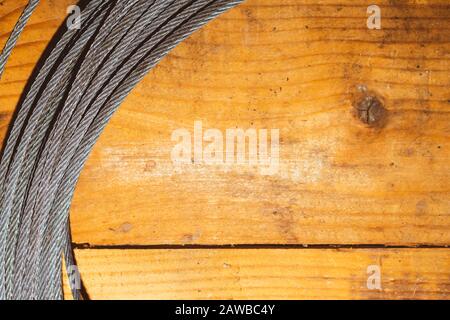 Stahlkabel auf Holzhintergrund. Hank aus Metallseil liegt auf dem Tisch. Arbeitswerkzeug Stockfoto