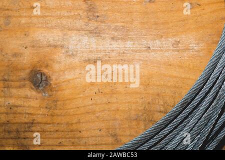 Stahlkabel auf Holzhintergrund. Hank aus Metallseil liegt auf dem Tisch. Arbeitswerkzeug Stockfoto