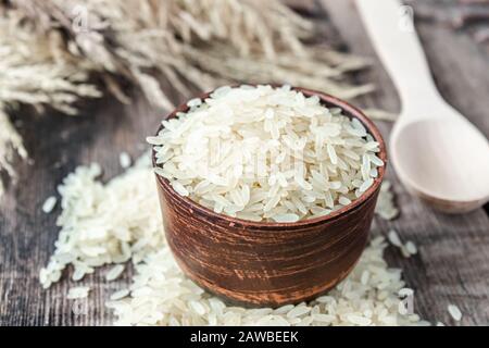 Eine Schüssel mit weißem Reis neben einem Reishaufen auf einem Hintergrund alter Bretter. Jasminreis zum Kochen. Nahaufnahme. Stockfoto