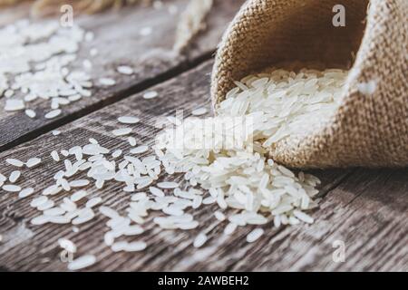 Weißer Reis aus einem Beutel auf einem Hintergrund alter Bretter verstreut. Jasminreis zum Kochen. Nahaufnahme. Stockfoto