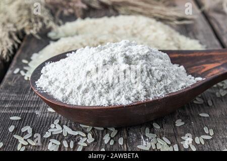 Reismehl in einem Löffel neben weißem Reis auf alten Bretter. Jasminreis zum Kochen. Stockfoto