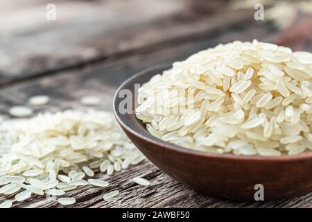 Eine Schüssel mit weißem Reis vor dem Hintergrund alter Bretter in der Nähe von bestreutem Reis. Jasminreis zum Kochen. Nahaufnahme. Stockfoto