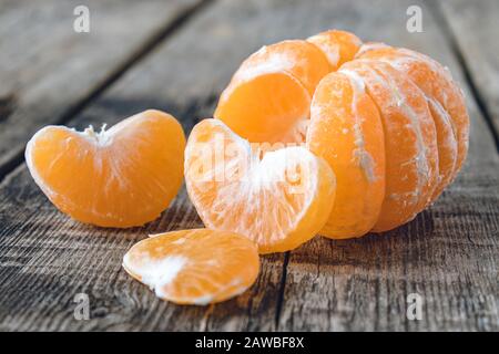Reif geschälte Tangerine ohne Schale liegt auf dem Tisch neben Stücken reifer Tangerine. Citruszangen oder Orangen. Nahaufnahme. Stockfoto