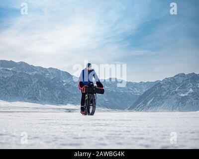 Reisende fahren mit einem fetten Fahrrad auf dem Eis eines gefrorenen Bergsees. Reisen im Winter. Extreme Expedition. Stockfoto