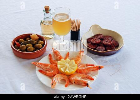 Eine Auswahl an Tapas mit Bier, King-Garnelen mit Zitrone, Chorizo-Wurst in Scheiben und grünem Olivencocktail, Costa del Sol, Spanien. Stockfoto