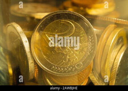 Münzen verschiedener Länder in einem Glasbecher. Viele Metallmünzen verschiedener Stückelungen und verschiedener Länder. Finanzieller Hintergrund. Euro-Münze in Stockfoto