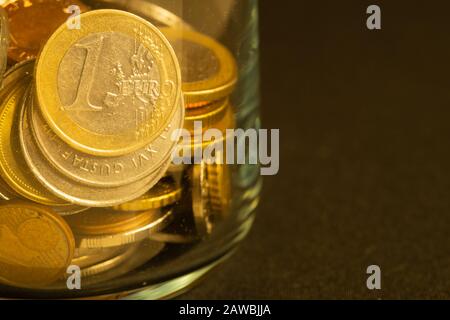 Münzen verschiedener Länder in einem Glasbecher. Viele Metallmünzen verschiedener Stückelungen und verschiedener Länder. Finanzieller Hintergrund. Euro-Münze in Stockfoto