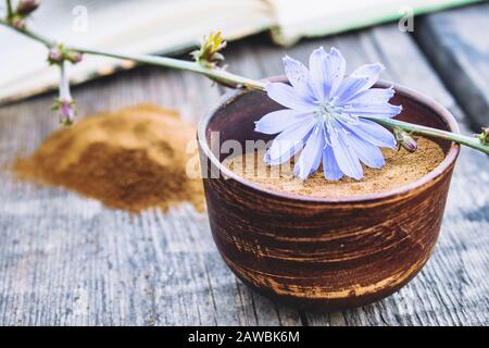 Blaue Zichorienblume und eine Schüssel mit Instant-Zichorienpulver auf einem alten Holztisch. Zichorienpulver. Das Konzept des gesunden Essens eines Getränks. Kaffee substit Stockfoto