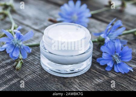 Blaue Zichorienblume und Gesichtscreme in einem Glasbecher auf einem alten Holztisch. Gesundheitskonzept. Whirlpool Stockfoto