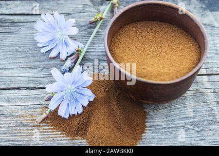 Blaue Zichorienblume und eine Schüssel mit Instant-Zichorienpulver auf einem alten Holztisch. Zichorienpulver. Das Konzept des gesunden Essens eines Getränks. Kaffee substit Stockfoto