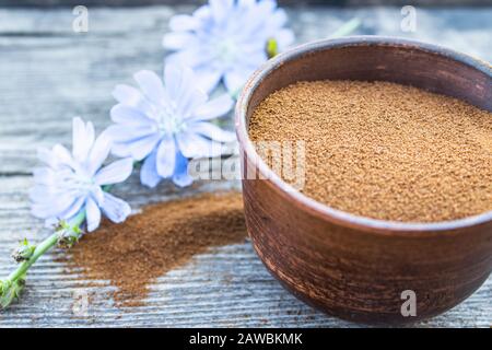 Blaue Zichorienblume und eine Schüssel mit Instant-Zichorienpulver auf einem alten Holztisch. Zichorienpulver. Das Konzept des gesunden Essens eines Getränks. Kaffee substit Stockfoto